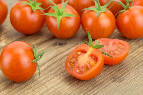 Haufen Kirschtomaten und eine halbierte Tomate, auf hölzerner Oberfläche. — Stockfoto