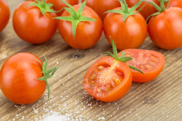 Haufen Kirschtomaten mit einer halbierten Tomate und einer Prise Salz auf einer Holzoberfläche. — Stockfoto