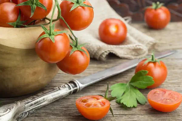 Montón de tomates cherry en tazón, con cuchillo y algunos cortados por la mitad, sobre superficie de madera . — Foto de Stock