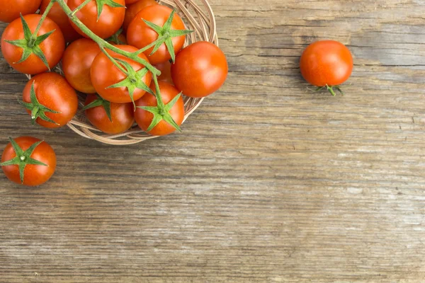 Montón de tomates cherry en cuenco de mimbre, en la superficie de madera con espacio de copia — Foto de Stock