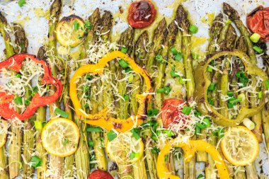 Limon dilimleri, cherry domates, dolmalık biber halkaları ve vegan parmesan peyniri ile kavrulmuş kuşkonmaz spears.