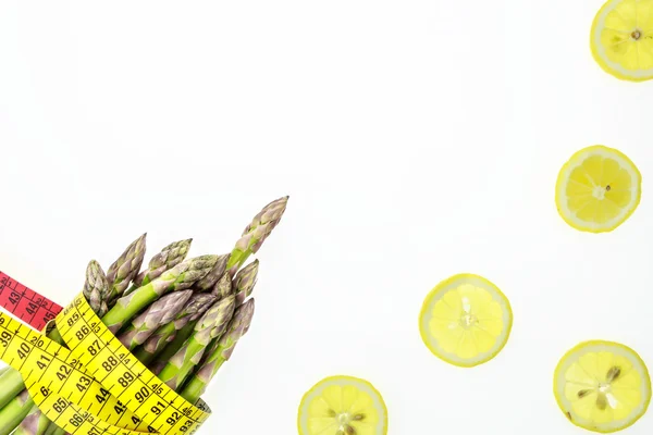 Lanças de espargos com fita métrica e fatias de limão, em fundo branco com espaço de cópia — Fotografia de Stock