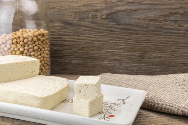 Tofu y soja en jarrón, sobre fondo de madera . — Foto de Stock