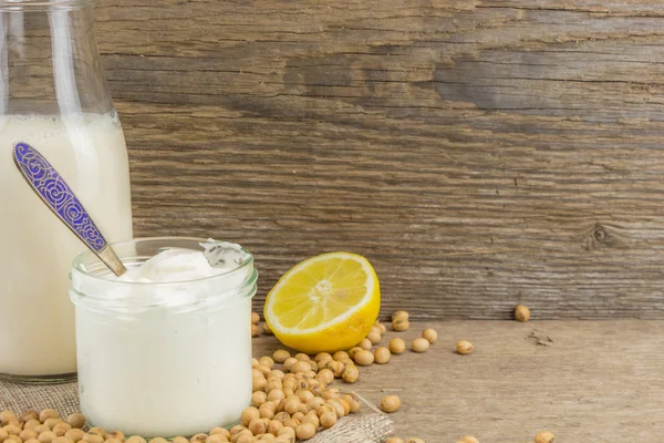 Bottle of soy milk, soy mayonnaise and lemon with soybeans, on wooden background