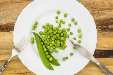 Ahşap yüzey üzerinde çatal ve bıçak closeup ile plaka üzerinde taze yeşil bezelye