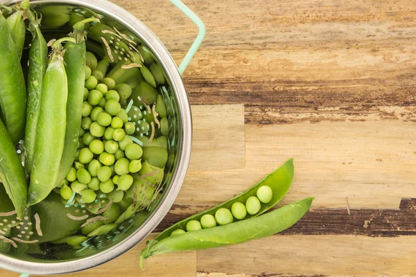 Verse doperwtjes in vergiet, op houten oppervlak — Stockfoto