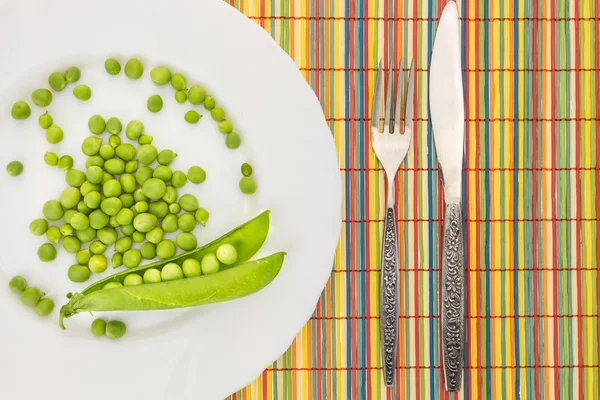 Fresh green peas on plate with fork and knife closeup, on colorful bamboo placemat — Stock Photo, Image
