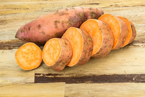 Verse zoete aardappelen geheel en gesneden, op houten achtergrond — Stockfoto
