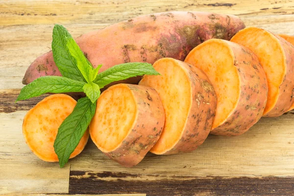 Batatas doces frescas inteiras e fatiadas, sobre fundo de madeira — Fotografia de Stock