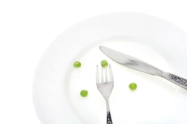 Piselli verdi freschi su piatto con forchetta e coltello primo piano, su fondo bianco — Foto Stock