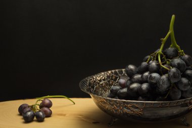 Üzüm, ahşap yüzey ve siyah arka plan üzerinde küme ile antika meyve kase 