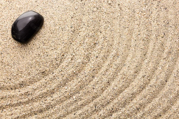 Черный базальтовый камень на песке имитирует колебания воды — стоковое фото
