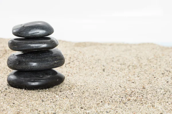 Pila di basalto nero pietre equilibranti su sabbia, su fondo bianco . — Foto Stock