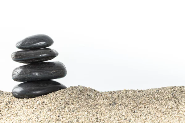 Pilha de pedras de balanço de basalto preto na areia, no fundo branco . — Fotografia de Stock
