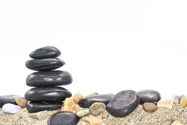 Stapel zwart basalt balancing stenen op zand, op witte achtergrond. Stockfoto