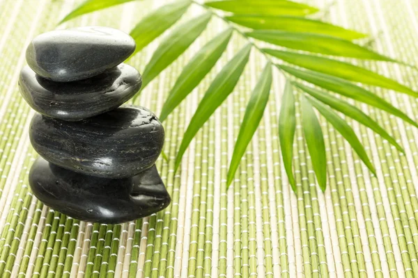 Pilha de pedras de equilíbrio de basalto preto com folha verde no tapete de bambu — Fotografia de Stock