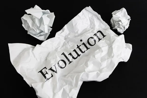 Hoja de papel arrugada con palabra Evolution aislada en negro — Foto de Stock