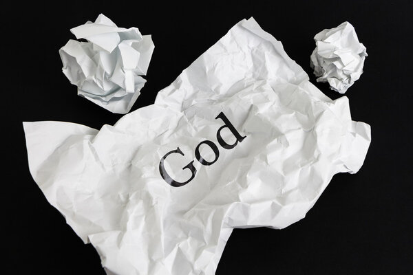 Crumpled paper sheet with word God isolated on black