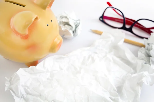 Piggy bank met sommige verfrommeld papier, brillen en potlood. — Stockfoto