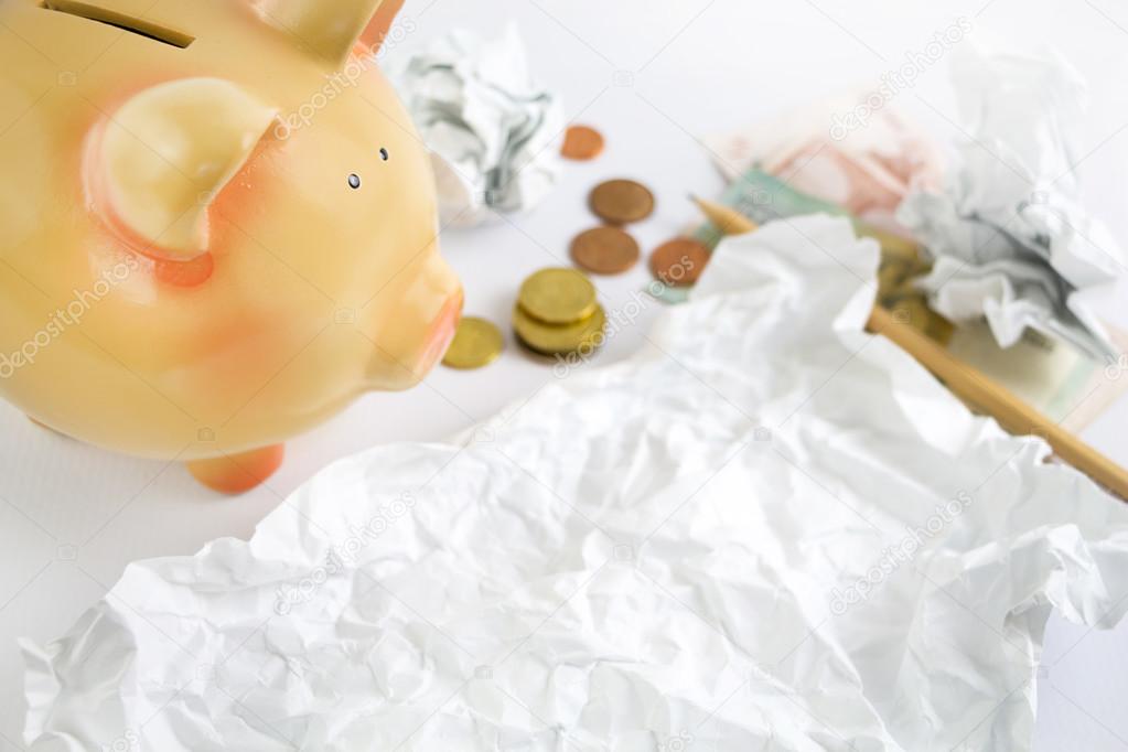 Piggy bank with some crumpled paper, money and pencil.