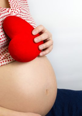 Kırmızı kalp karnı üzerinde tutan hamile kadın