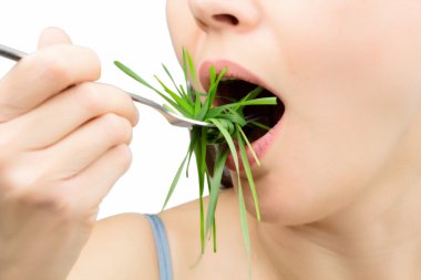Woman with fork eating wheatgrass as spaghetti, isolated on white. clipart