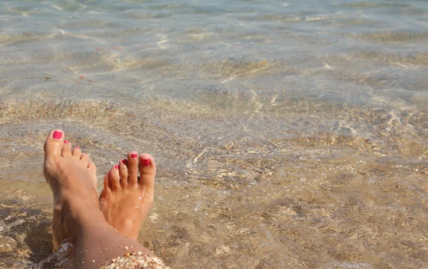 Natte vrouwelijke voeten door water op een strand — Stockfoto