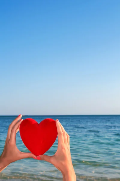 Händer som håller rött hjärta med blå himmel och hav horisonten i bakgrunden. — Stockfoto