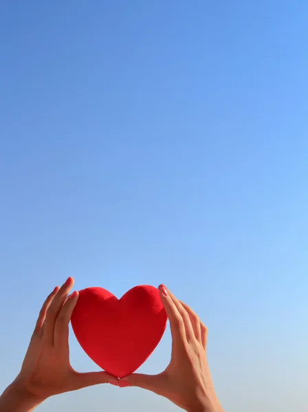 Manos sosteniendo el corazón rojo con cielo azul claro y espacio de copia — Foto de Stock