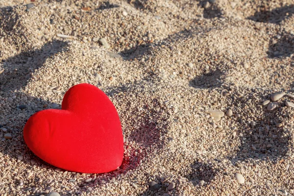 Rotes Herz am Strand mit kleinen Kieselsteinen Hintergrund. — Stockfoto