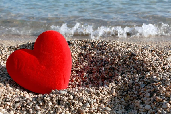 Corazón rojo sobre pequeños guijarros junto al fondo del mar . — Foto de Stock