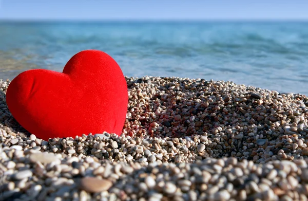 Corazón rojo sobre pequeños guijarros junto al fondo del mar . — Foto de Stock