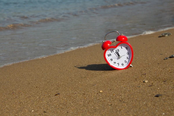 Rode klok in de vorm van hart op een zandstrand achtergrond. — Stockfoto