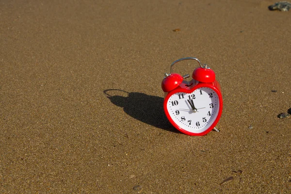 Czerwony zegar w kształcie serca na tle piaszczystej plaży. — Zdjęcie stockowe