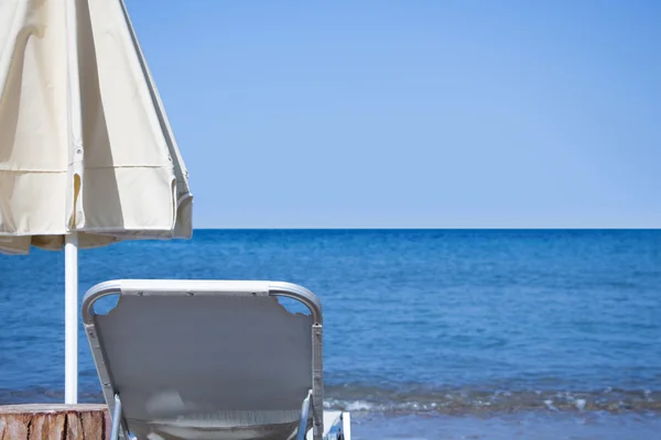 White sunbed and white closed parasol infront of blue sky and sea horizon. — Stock Photo, Image