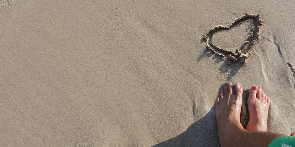 Fundo de areia molhada com pés de homem e mulher e coração desenhando na areia . — Fotografia de Stock