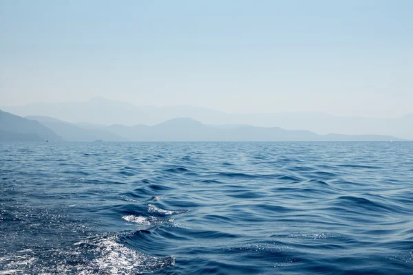 Paisaje marino con montañas lejanas, cielo y agua de mar ondulada — Foto de Stock