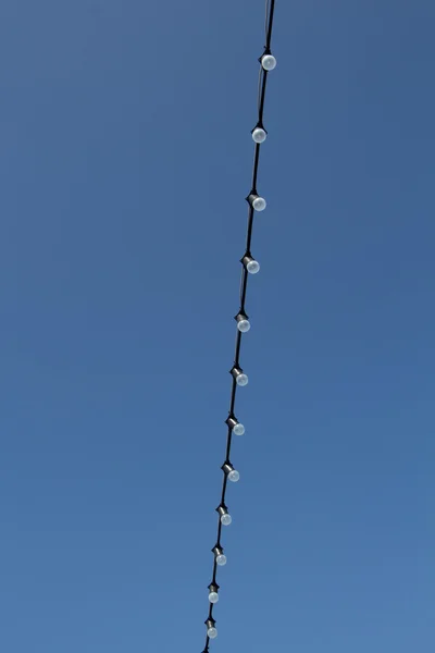 Cordón con una fila de bombillas encendidas contra el cielo azul —  Fotos de Stock