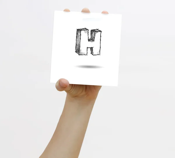 Hand holding a piece of paper with sketchy capital letter H, isolated on white. — Stock fotografie