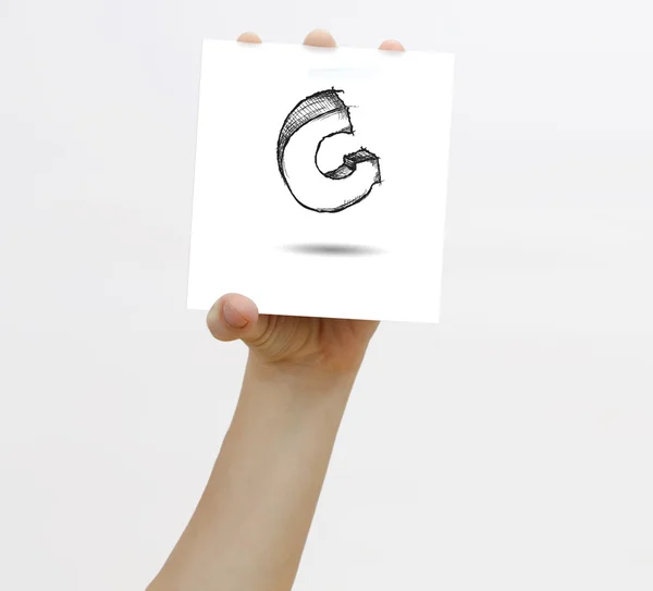 Hand holding a piece of paper with sketchy capital letter G, isolated on white. — Stock Photo, Image