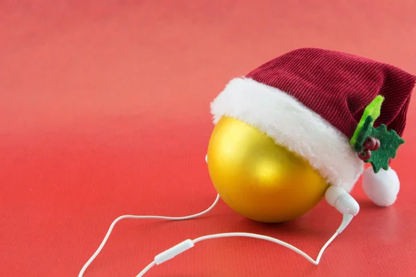 Christmas ball with Santa's hat and earphones, on red with copy-space — Stock Photo, Image