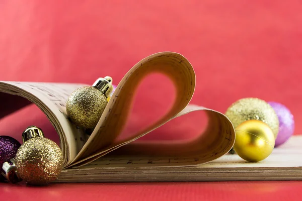 Music notation book with pages shaping heart and Christmas ornaments — Stock Photo, Image