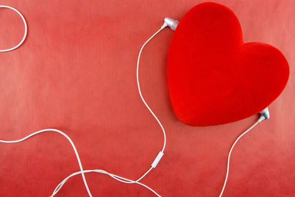 Heart with earphones closeup on red background — Stock Photo, Image