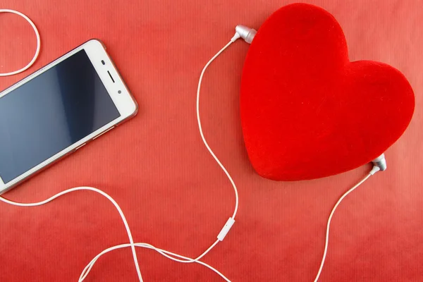 Heart with smartphone and earphones closeup on red — Stock Photo, Image
