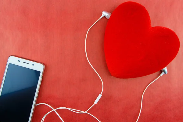 Heart with smartphone and earphones closeup on red — Stock Photo, Image