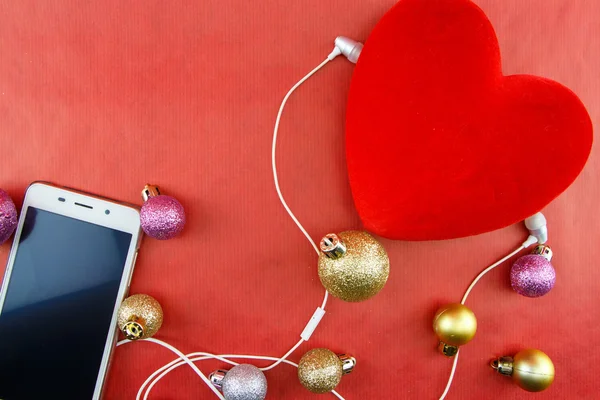 Coração com enfeites de Natal e smartphone com fones de ouvido, em vermelho com espaço de cópia — Fotografia de Stock