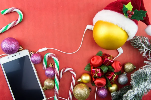 Bola de Natal com chapéu de Papai Noel e smartphone com fones de ouvido, em vermelho com espaço de cópia — Fotografia de Stock
