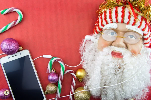 Santa with smartphone and earphones, on red with Christmas ornaments — Stock Photo, Image