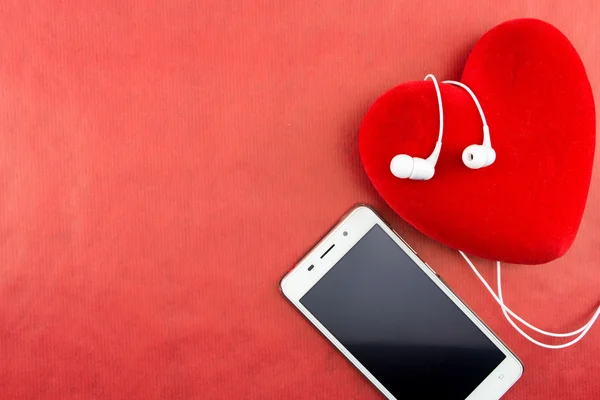 Heart with smartphone and earphones closeup on red with copy-space — Stock Photo, Image