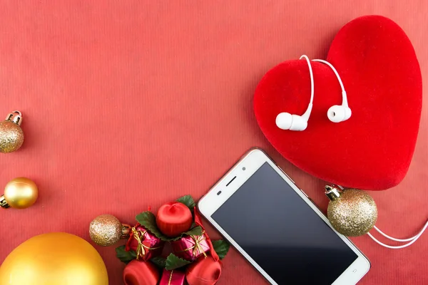 Coração com enfeites de Natal e smartphone com fones de ouvido, em vermelho com espaço de cópia — Fotografia de Stock